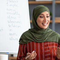 teacher in headscarf explaining English grammar rules to students.