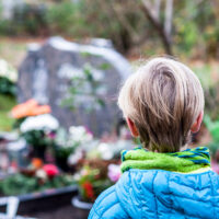 Little boy standing at the grave of his parents in the graveyard