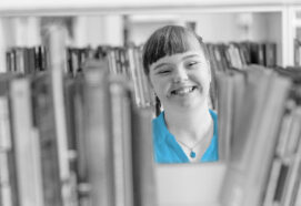 Girl with ID chooses a book on a shelf in the library. Education for disabled children