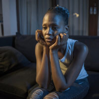 African American girl at night suffering depression - young attractive sad and depressed black woman lying thoughtful feeling sick on sofa couch in pain and worry