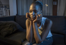 African American girl at night suffering depression - young attractive sad and depressed black woman lying thoughtful feeling sick on sofa couch in pain and worry