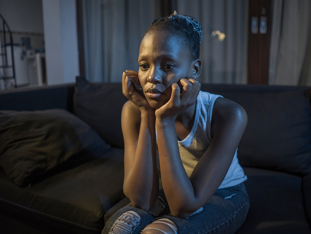 African American girl at night suffering depression - young attractive sad and depressed black woman lying thoughtful feeling sick on sofa couch in pain and worry