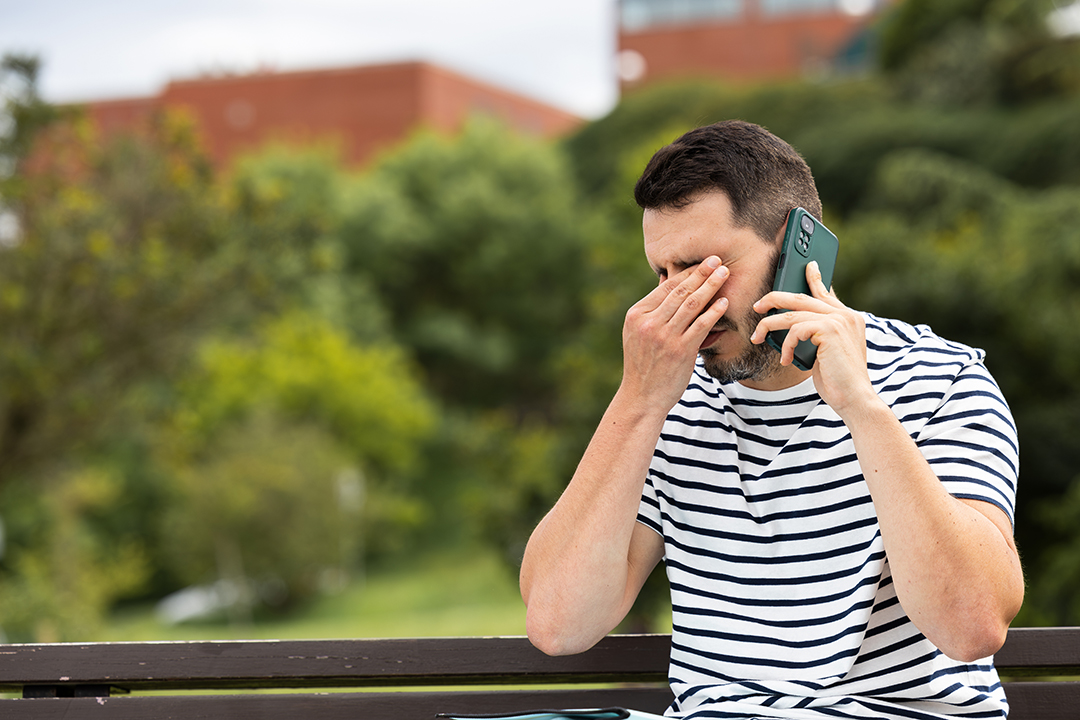 sad young man receives bad news on the phone sitting alone on a park bench