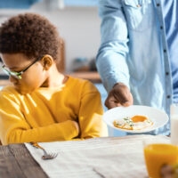 Fussy eater. Pouting pre-teen boy sitting at the table and turning away while refusing to eat a fried egg