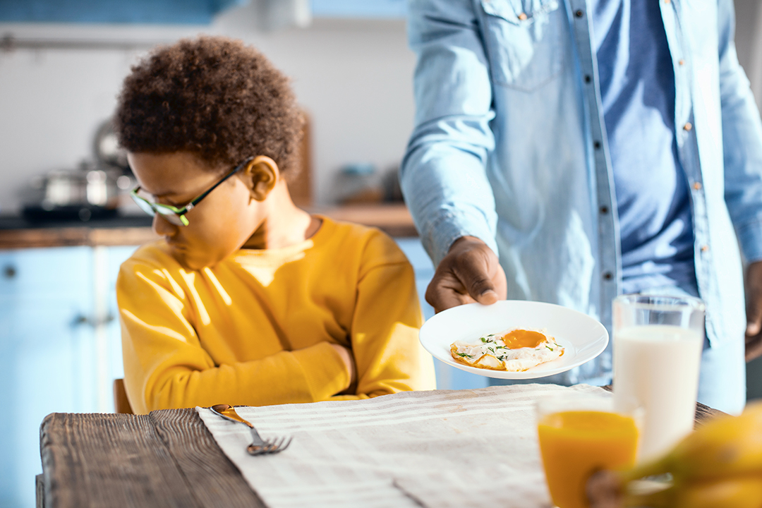 Fussy eater. Pouting pre-teen boy sitting at the table and turning away while refusing to eat a fried egg