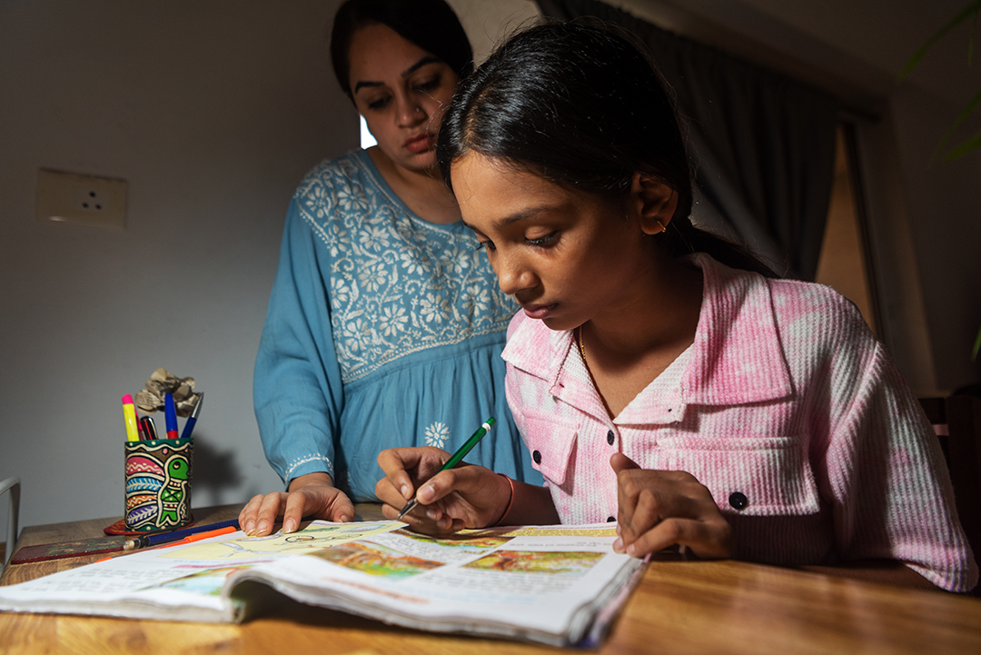 An Indian mother, wearing a blue chikankari kurta, supervises her pre-teen daughter's homework in the evening after returning from work at their home in Mumbai, India.
