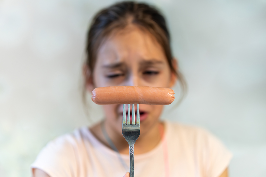 not Delicious fast junk food. Close-up. A teenage girl looks at a boiled sausage with dislike. Tasteless fast food.