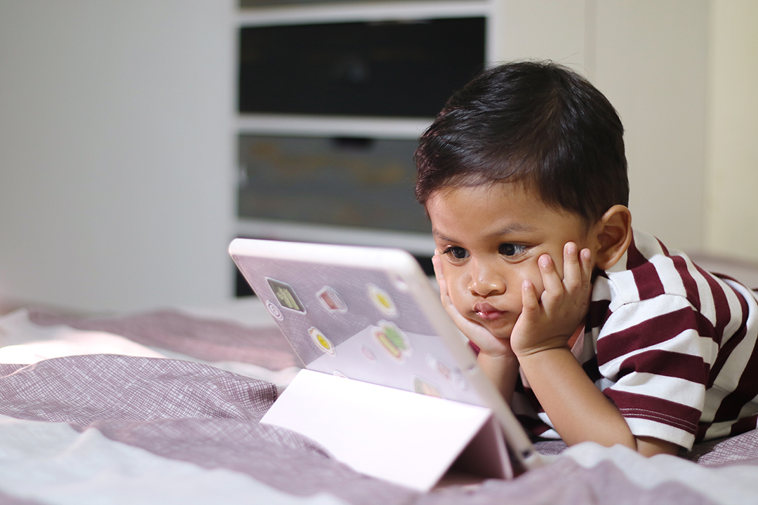 three year old Asian boy at home bed using digital tablet computer