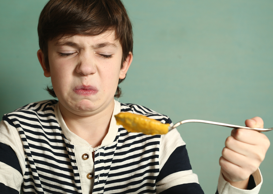 preteen boy eating pumpkin vegetable soup with disgust expression grimace close up photo