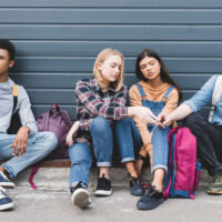 teenagers sitting, drinking beer from glass bottle and holding cigarette