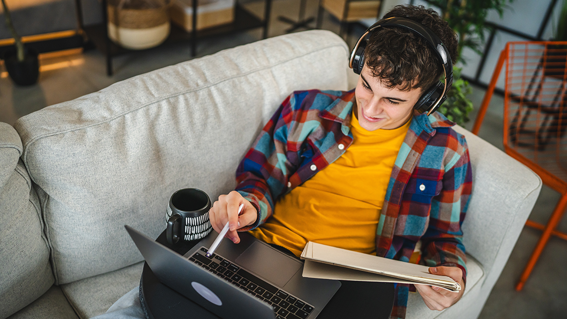 boy on reclined on sofa with laptop on lap and headphones on
