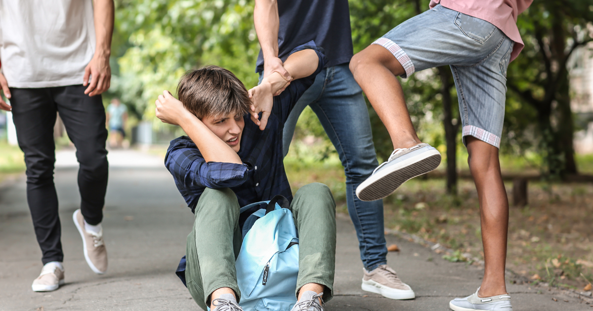 Aggressive teenagers bullying boy outdoors