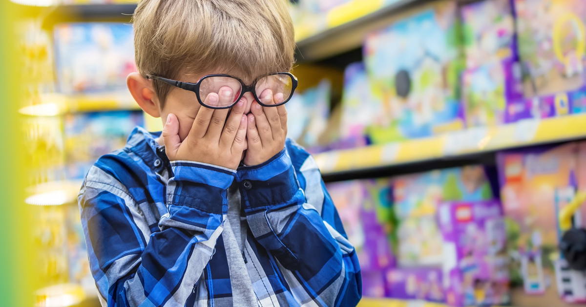 young boy in a toy shop wearing glasses upset with hands over eyes crying