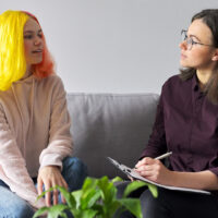 teen girl with bright yellow hair giving interview to female psychiatrist