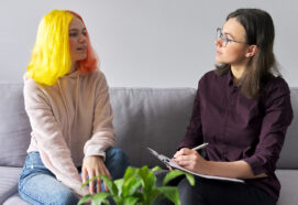 teen girl with bright yellow hair giving interview to female psychiatrist