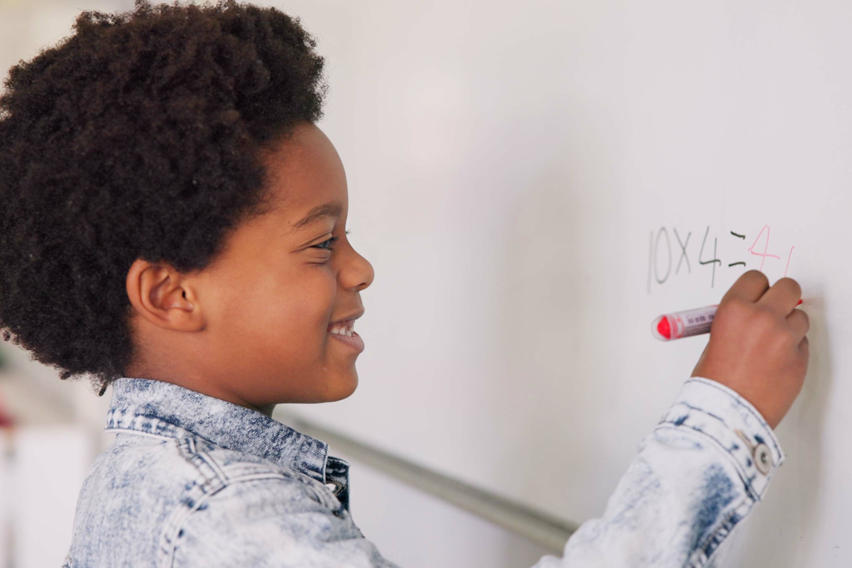 Math class, happy child at board for education, learning and problem solving for skill development. Boy writing on whiteboard in classroom with solution, thinking and smile at school for knowledge.