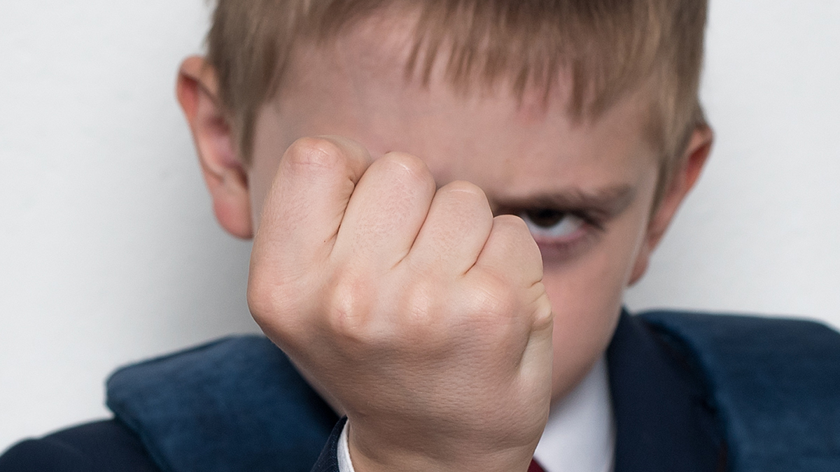 Schoolboy threatens with his fist. Boy in school uniform. White background. Brawler