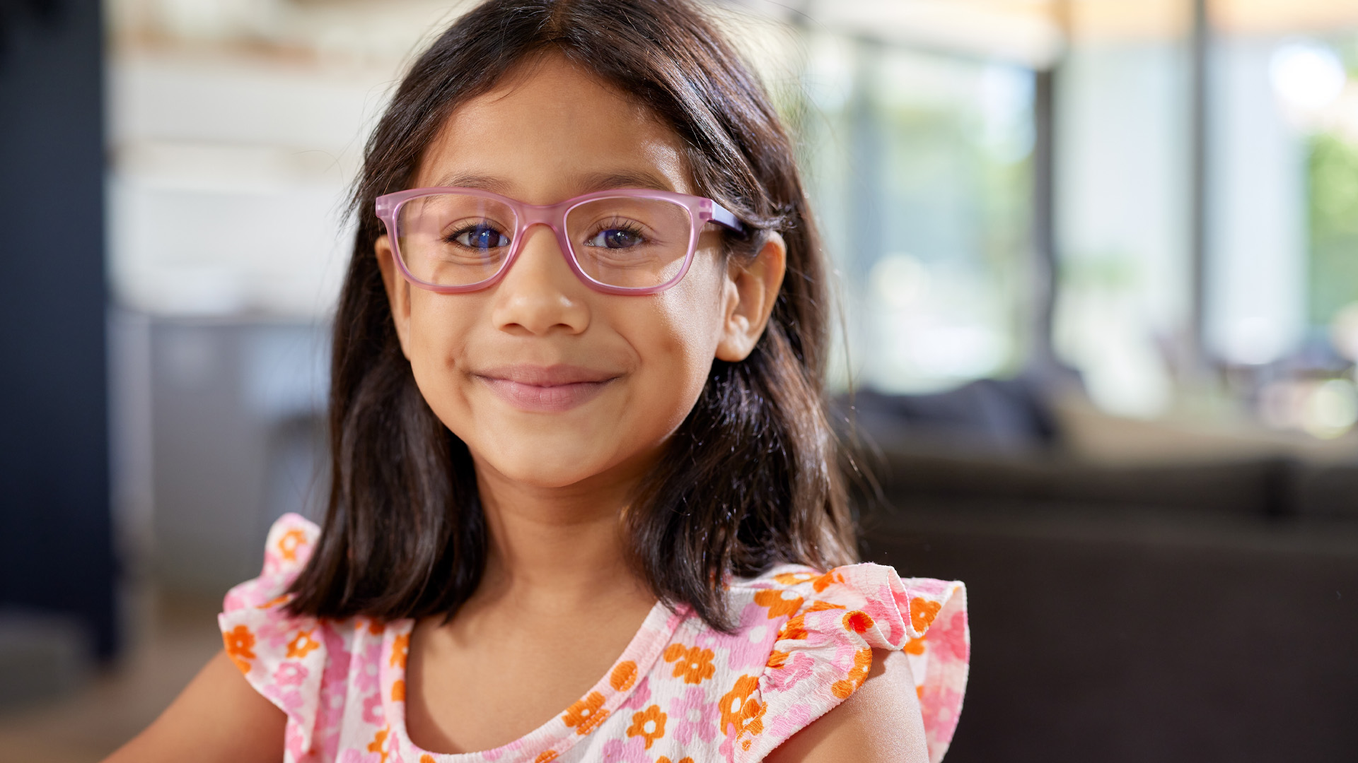 A young indian girl wearing glasses and a floral t-shirt while smiling at camera in a cozy home A young indian girl wearing glasses and a floral t shirt while smiling at camera in a cozy home