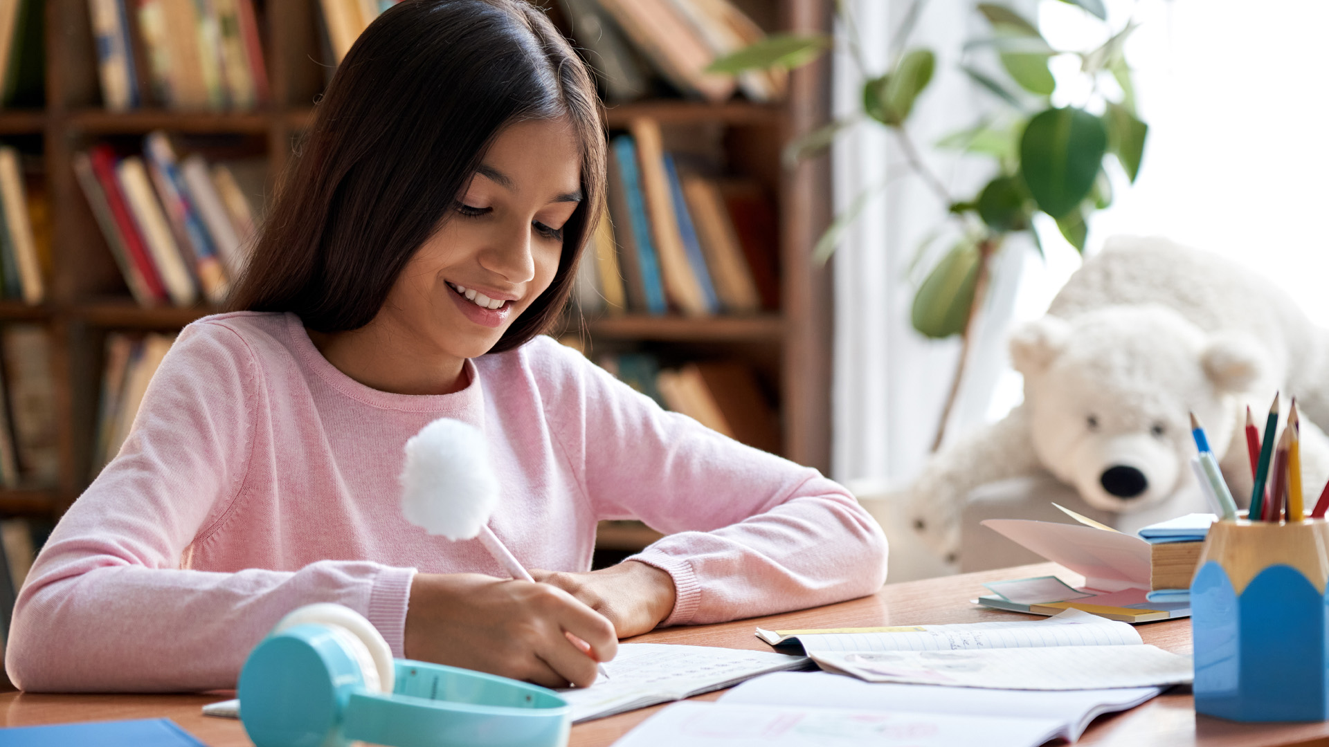 Happy smiling indian preteen school girl pupil studying at home sitting at desk. Happy smiling indian preteen school girl pupil studying at home sitting at desk.