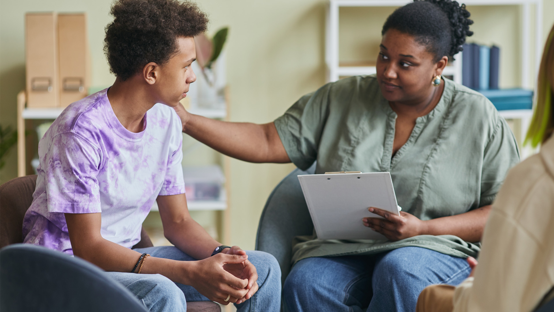 young psychologist talking to teenage boy during therapy session