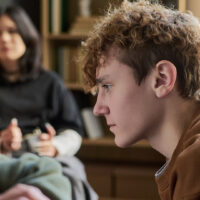 Teenager boy sitting in profile listening attentively within a group with multiethnic young people and teenagers in background participating in discussion