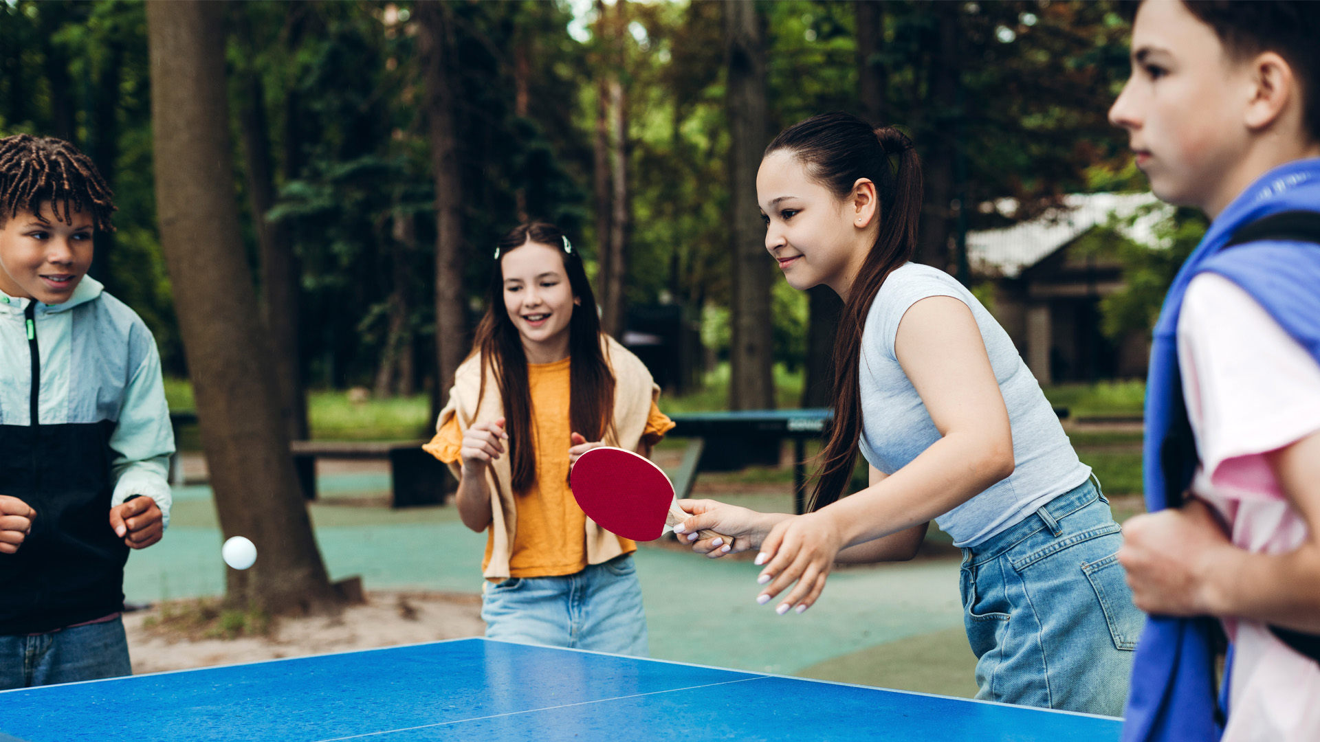 Group of happy teenagers playing table tennis outdoors in a green park. Group of happy teenagers playing table tennis outdoors in a green park.