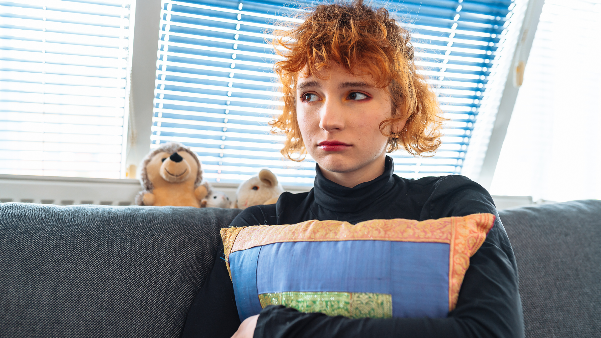 portrait teenage girl, with red curly hair, sitting on sofa, hugging pillow, 