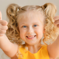 Close up portrait of nice cute cheerful small little girl, showing double thumbs up
