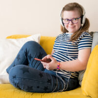 Portrait of Teenage girl with Down syndrome listening to music in headphones sitting on sofa at home