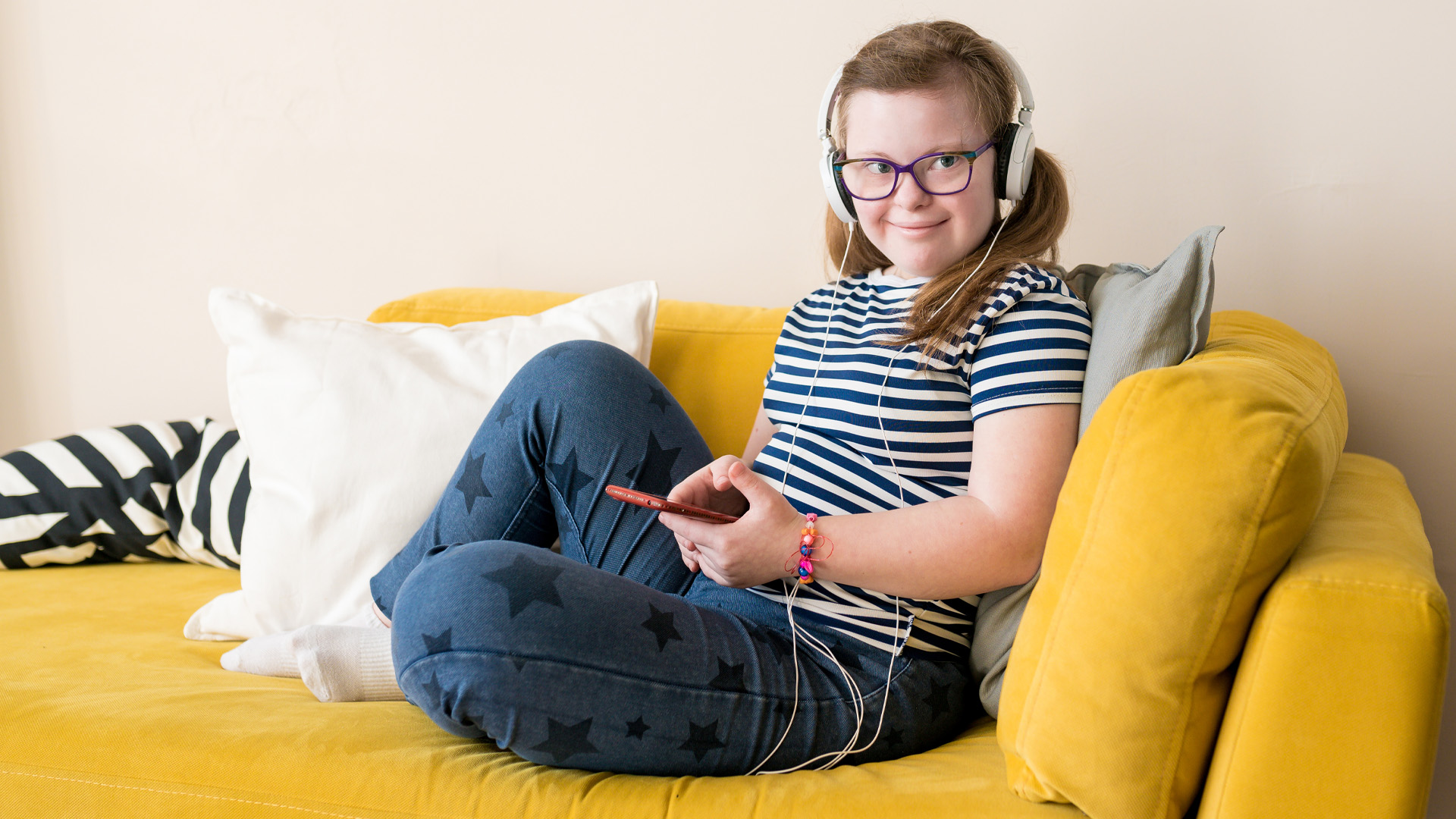 Portrait of Teenage girl with Down syndrome listening to music in headphones sitting on sofa at home
